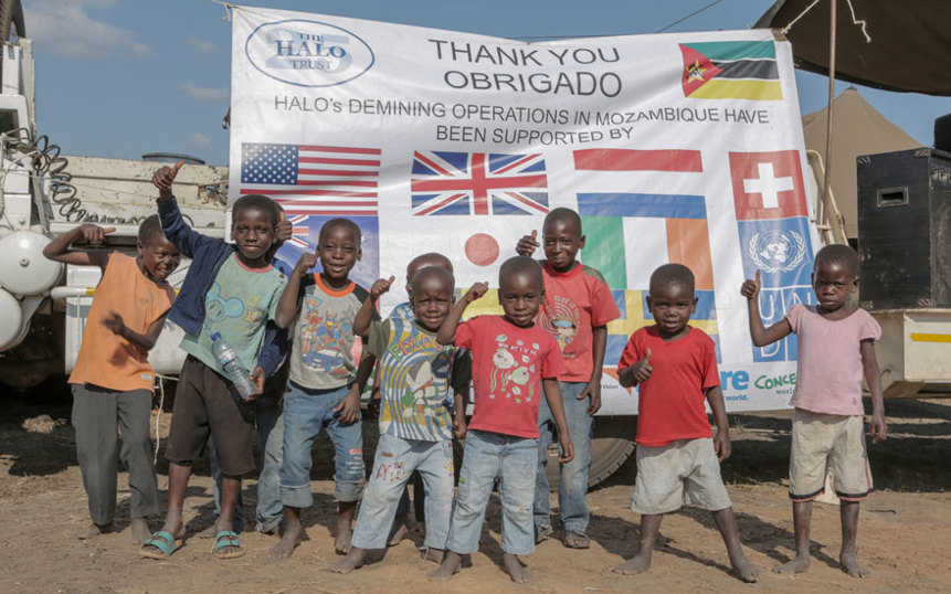Children smile in front of a sign celebrating Mozambique's mine-free status