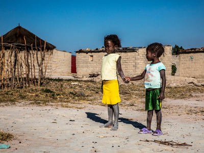 Two children hold hands outside of a house in the village of Lusserei Village, Angola