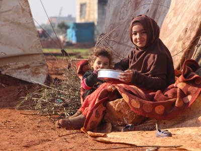 A child and a toddler sit on the ground holding a metal bowl