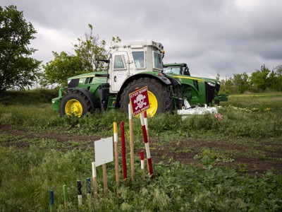 A large agricultural machine stands in the middle of a field behind a landmine warning sign.