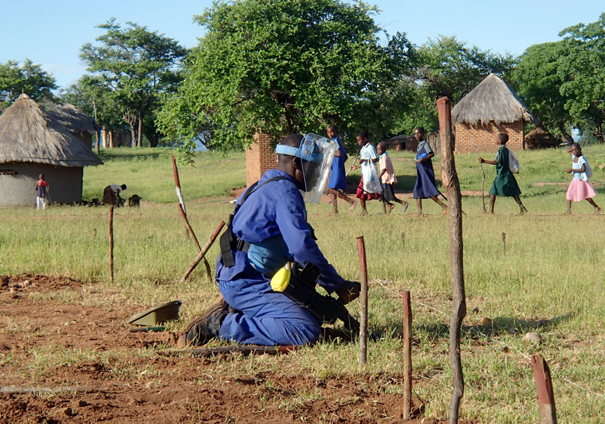 A deminer wearing PPE digs in mine marked soil