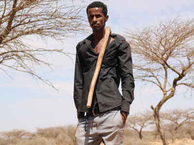 Abdul Nasser a goat herder in Somaliland stands with a walking stick over his shoulder 