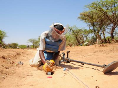 A deminer excavates a signal in PPE and a visor in Somalia