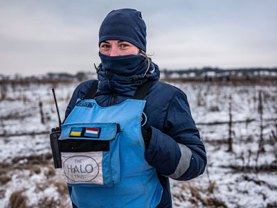 A deminer wearing PPE poses in a snowy minefield