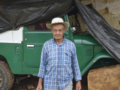 A Colombian farmer stands in front of a large jeep like vehicle