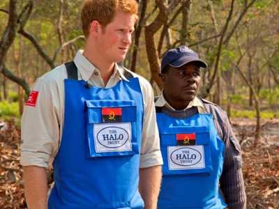 Prince Harry stands next to a HALO staff member wearing protective gear with an Angola badge 