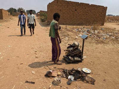  A child in a rural area weighs a bunch of scrap metals on a scale outside