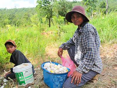 A mother and son crouch next to two baskets filled with mushrooms outside