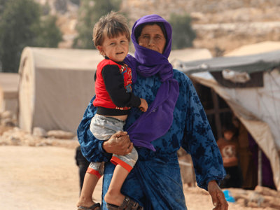 A woman holds a child in the middle of a street with tents in the background