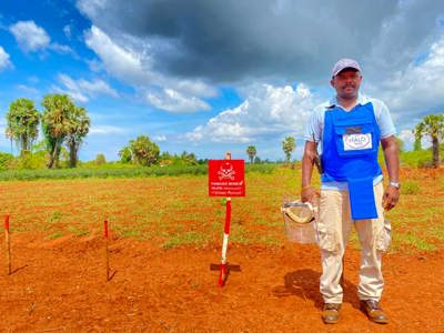 Balamuralee Balasingam stands in front of a Danger Mines sign in a minefield in Sri Lanka