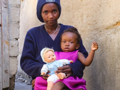 HALO worker, Rebeca Cupenala, sits with her daughter on her lap whilst holding a doll