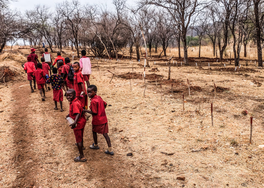 A group of school children in red uniforms walking through a minefield in Zimbabwe