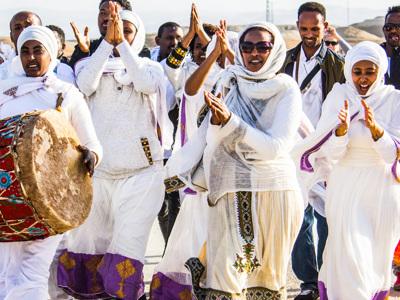 A group of people play drums and dance in white cloth outside