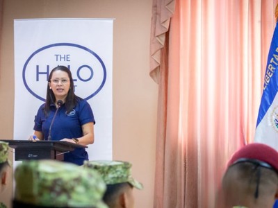 Deysi stands at a lectern wearing a HALO top in front of military personnel