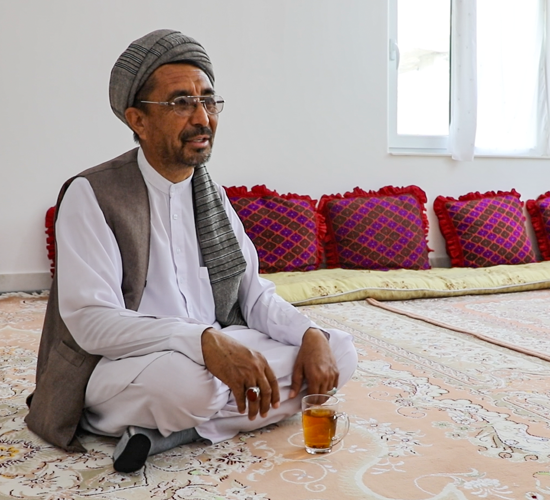 Mohammed Mirzayee, sits cross legged with a mug of tea on a rug