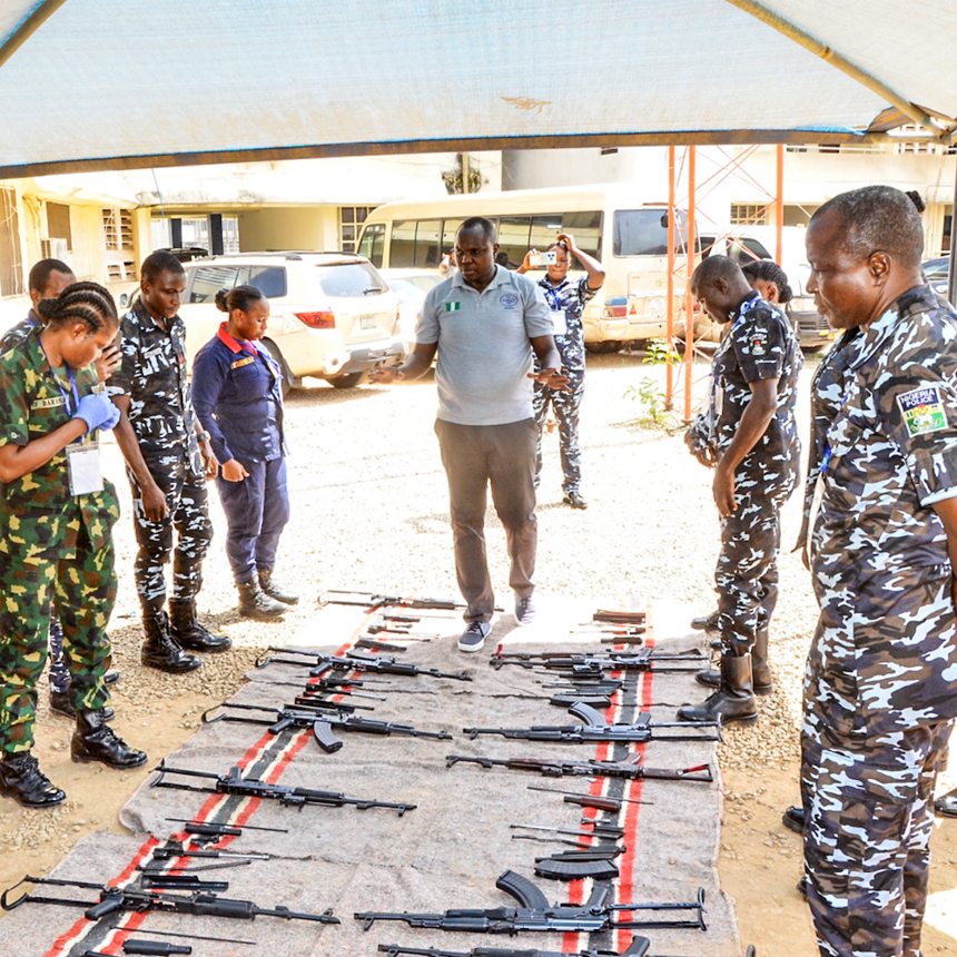 A HALO staff member speaks to the Nigerian police force as they stand by weapons on the ground