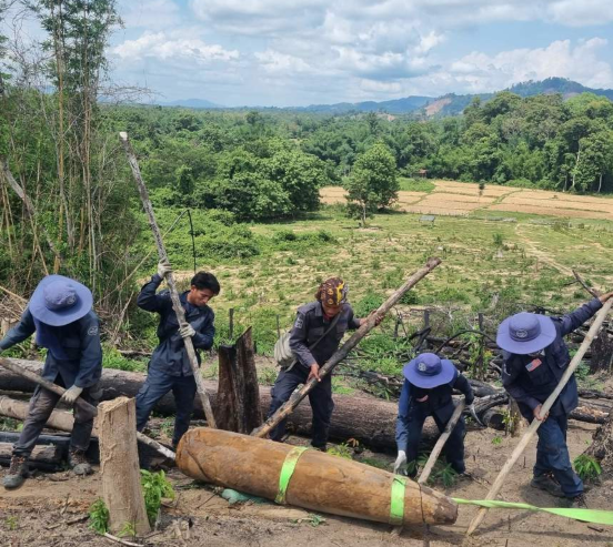 A group of HALO staff working with a large bomb in a field in Laos