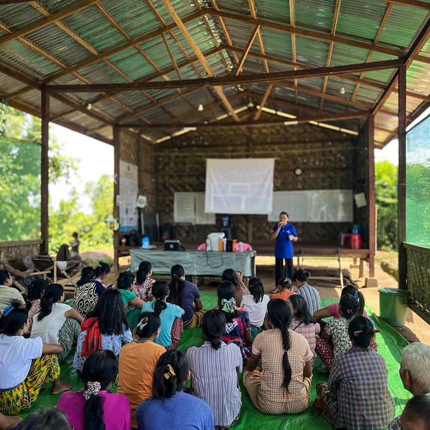 Women sitting on the floor of a tarpaulin-roofed classroom receive risk education sessions in Myanmar.