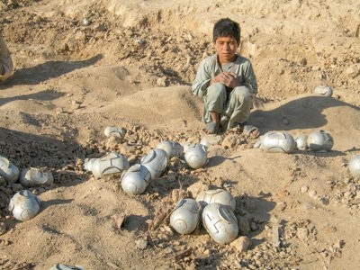 Boy squatting next to cluster munitions in Afghanistan
