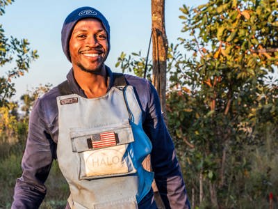 A male deminer wearing HALO uniform with a USA badge smiles