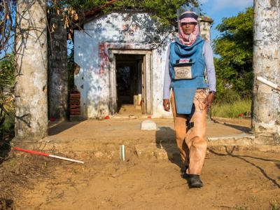 A woman wearing PPE stands in front of an old building with pillars