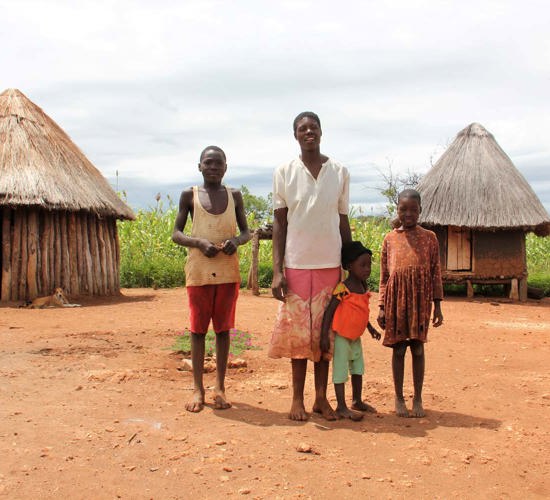 A family stand in front of some huts outside