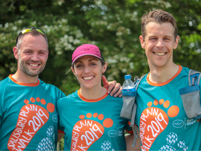 Three people smile and link arms as they wear T-shirts saying "Sailsbury plain walk 2019"